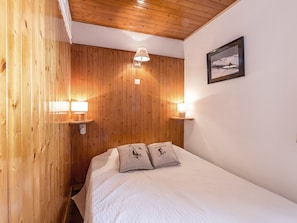 A wooden-paneled room with a bed, two wall-mounted lamps, and a framed picture on the wall.