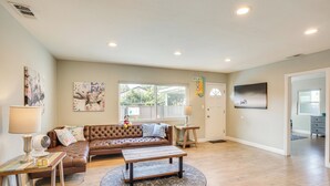 A spacious living room with a brown leather sofa, a wooden coffee table, and a large window.
