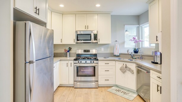 A modern kitchen with white cabinets, stainless steel appliances, and a wooden floor.