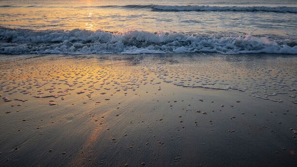 A beach at sunset with waves, a ship in the distance, and footprints on the sand. - Laurel Reef | Pet Friendly, Charming Home! (Tybee Island)
