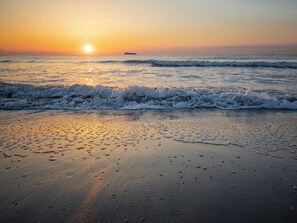 A beach at sunset with waves, a ship in the distance, and footprints on the sand. - Laurel Reef | Pet Friendly, Charming Home! (Tybee Island)