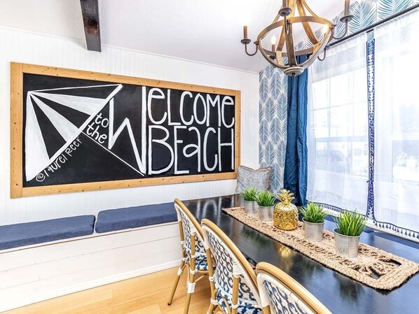 A dining area with a blackboard sign reading "WELCOME to the BEACH" and a modern chandelier. - Laurel Reef | Pet Friendly, Charming Home! (Tybee Island)