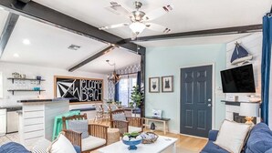 A modern living room with blue sofas, a coffee table, and a dining area with wicker furniture. - Laurel Reef | Pet Friendly, Charming Home! (Tybee Island)