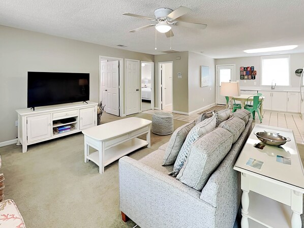 A living room with a television, sofa, ottoman, and a dining area with chairs and a table.