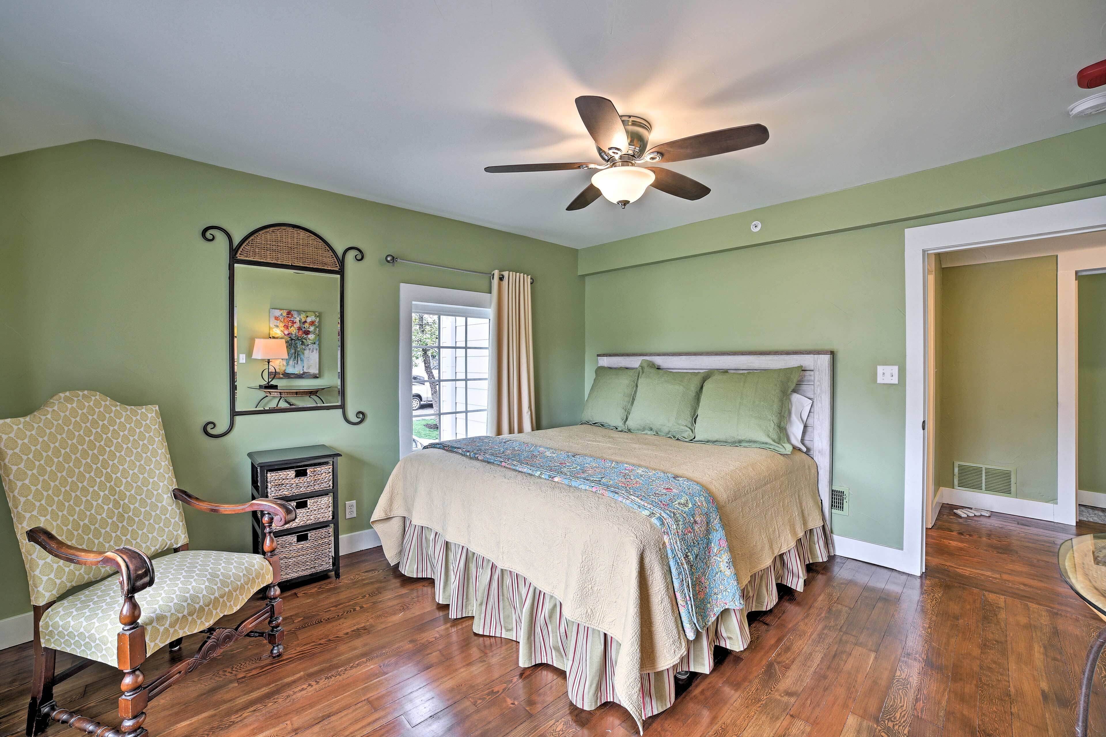 A bedroom with a bed, a chair, a dresser, a ceiling fan, and a window with curtains.