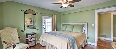 A bedroom with a bed, a chair, a dresser, a ceiling fan, and a window with curtains.