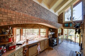 A kitchen with a brick wall, large windows, a stove, and a dining area with chairs and a table.