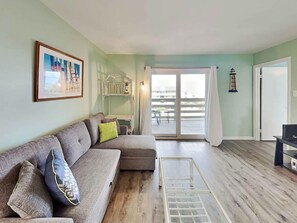 A living room with a grey sofa, a small white table, and a balcony with a view.