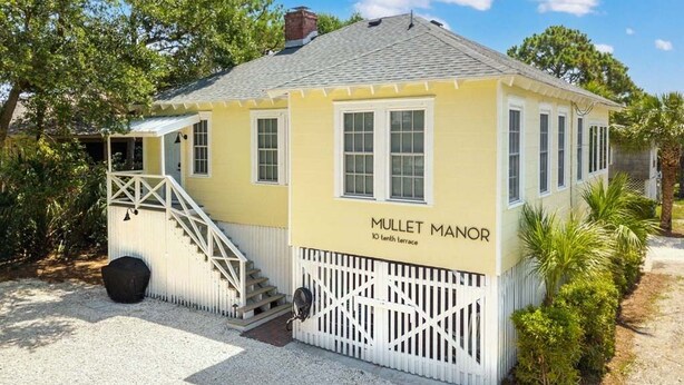 Een geel gebouw met de tekst 'MULLET MANOR', omringd door een witte hek en een trap naar de ingang.