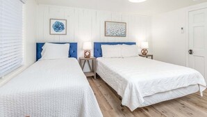 Een hotelkamer met twee eenpersoonsbedden, witte beddengoed, houten vloeren en een witte deur.