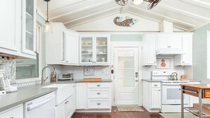A kitchen with white cabinets, a dishwasher, a stove, and a coffee maker. - Sunny Daze | Large Patio + Fire Pit! (Tybee Island)