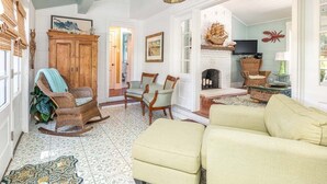A living room with a fireplace, wicker furniture, and a patterned rug. - Sunny Daze | Large Patio + Fire Pit! (Tybee Island)