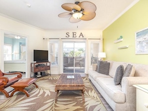 Relax in this inviting living space with a sofa, television, and ceiling fan, offering a view of the outdoors through the large window.