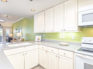 Kitchen features a sink, stove, and microwave, with ample counter space and a window with blinds.