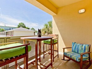 Relax on the balcony with a view of the water, surrounded by comfortable seating and lush greenery.
