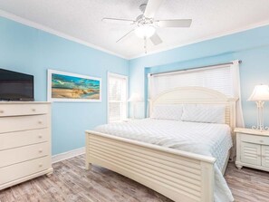 Un dormitorio con cama, cómoda, mesita de noche, ventilador de techo y un cuadro en la pared.