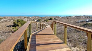 Une promenade en bois qui mène à une plage, avec un ciel dégagé.