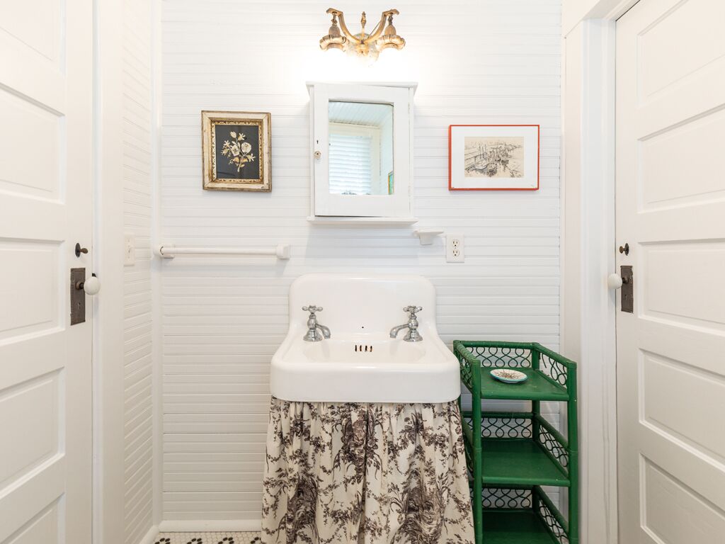A bathroom with white walls, a white sink, a green vanity, and two framed pictures on the wall.
