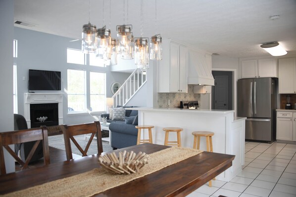 A modern kitchen with white cabinets, a stainless steel refrigerator, and a dining area with wooden chairs and a wooden table.