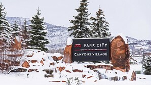 Schild für Park City Canyons Village, umgeben von schneebedeckten Bäumen und Felsen.