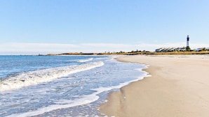 Une plage avec un phare visible au loin, un rivage sablonneux et une mer calme.