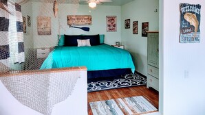 A bedroom with a turquoise bedspread, a ceiling fan, and fishing-themed wall art. - Lakefront/Wifi /Coffee/ Stocked Cabin /Kayaks /Beach/Firepit hammocks /Pet (Harrison)