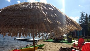 A beach with a thatched umbrella, red chairs, and a kayak. - Lakefront/Wifi /Coffee/ Stocked Cabin /Kayaks /Beach/Firepit hammocks /Pet (Harrison)
