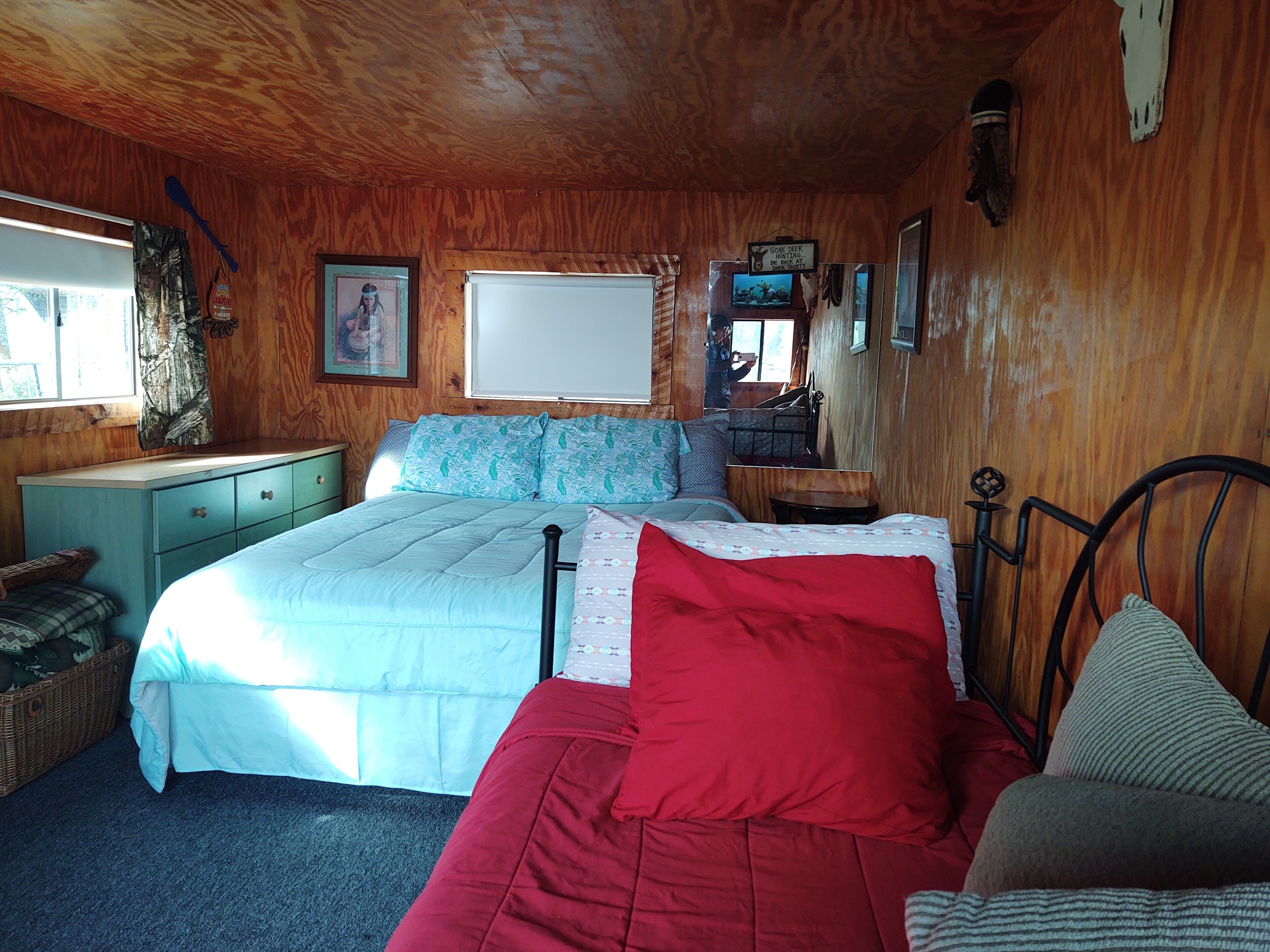 Une chambre confortable avec un plafond en bois, un lit recouvert d’une courtepointe rouge et blanche, une petite table et un miroir.