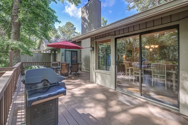Une terrasse couverte équipée d’un barbecue, de mobilier d’extérieur et d’une grande porte-fenêtre coulissante donnant sur un espace de repas intérieur.