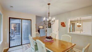 A dining room with a wooden table, white chairs, a chandelier, and a sliding glass door leading to a patio. - 4 Hollyberry - Dog Friendly.  Great Community Amenities (Hilton Head Island)