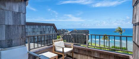 A wooden deck with a table and chairs, overlooking a beach and ocean.