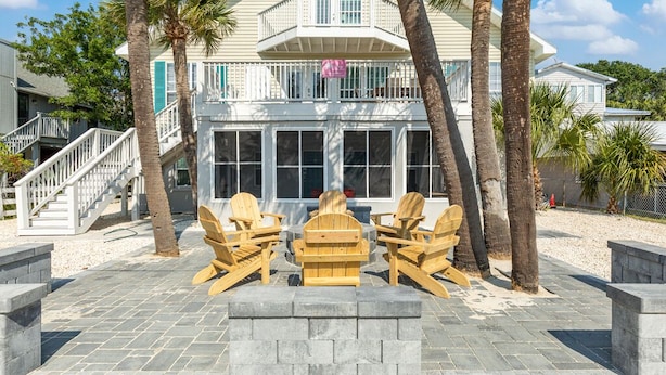 A beachfront property with a two-story house, a covered patio with Adirondack chairs, and a staircase leading to the entrance. - Dune B | Updated Ground Floor, Pet Friendly, 200 Yards to Beach (Tybee Island)