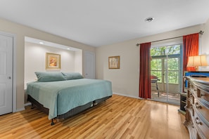 Ein Schlafzimmer mit einem Bett, Holzboden, einem Schminktisch, einem Fenster mit Vorhängen und einer Tür.