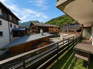Ein traditionelles Holzhaus mit Balkon, umgeben von einem Holzzaun und Blick auf einen bewaldeten Berg.