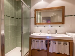 A bathroom with a glass shower enclosure, two sinks with mirrors, and a wooden vanity with towel racks.