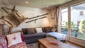 Et værelse med et monteret dyrhoved, en sofa, et bord og et vindue med udsigt til bygninger og træer.