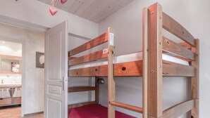 En køjeseng med rød madras i et rum med trægulv og en hvid dør.
