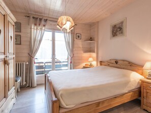 A wooden bedroom with a bed, a nightstand, a radiator, and a window with curtains.