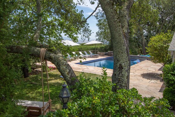 A backyard with a swimming pool, lounge chairs, and a swing.