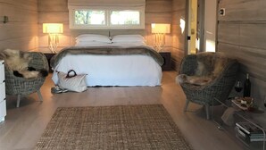 A bedroom with a large bed, two wicker chairs, a bedside table with a bottle and glasses, and a window with a view of trees. - Spa-like Estate, Wine Country Getaway, above the Sonoma Square, Amazing Views (Sonoma)
