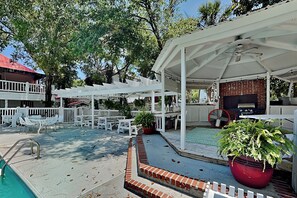 A covered outdoor area with a pool, white chairs, and a barbecue setup. - Tybreeza B | Apartment, Shared Pool, Near Beach! (Tybee Island)