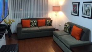 Un salon avec deux canapés, un téléviseur, une lampe et des tableaux encadrés accrochés au mur.
