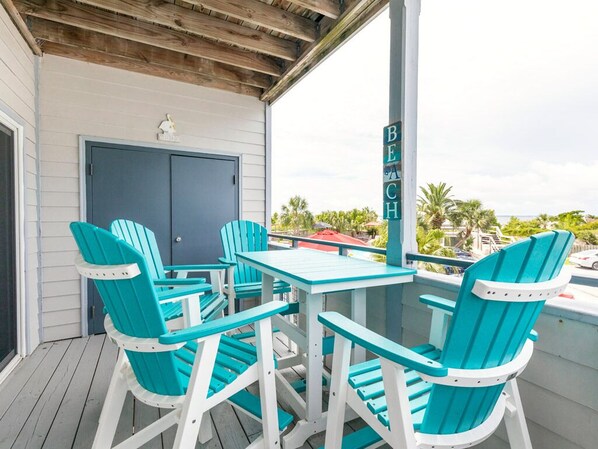 A covered outdoor seating area with turquoise chairs and a table, a door, and a sign reading "BEACH".
