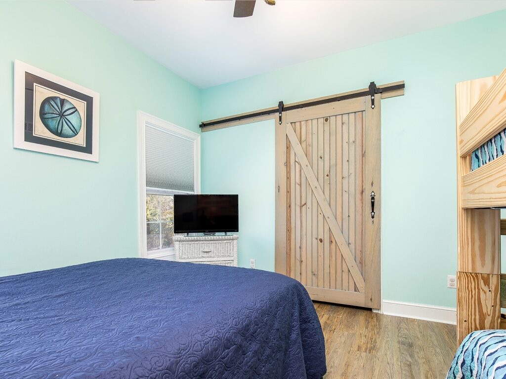 Ein Schlafzimmer mit Bett, Fernseher, einer Schiebetür im Scheunenstil und einem gerahmten Bild an der Wand.