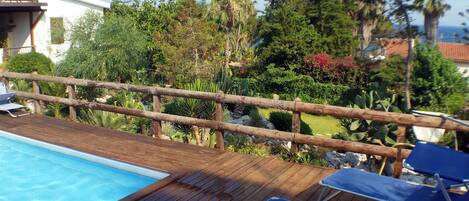 A wooden deck with a pool and lounge chairs.