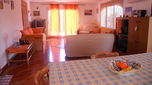 Una sala de estar acogedora con un sofá, una mesa de comedor con mantel a cuadros y un televisor.