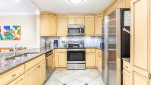 A modern kitchen with light wooden cabinets, stainless steel appliances, and a tiled floor. - Private Balcony, Community Pool, 30 Yards to Beach (Tybee Island)