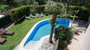 Une piscine à bord incurvé, entourée d’une pelouse bien entretenue et de plusieurs chaises longues.