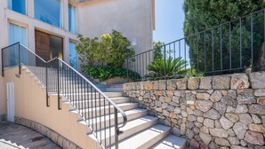 Un escalier en pierre menant à l’entrée d’un bâtiment, avec une rambarde en métal et un mur en pierre d’un côté.