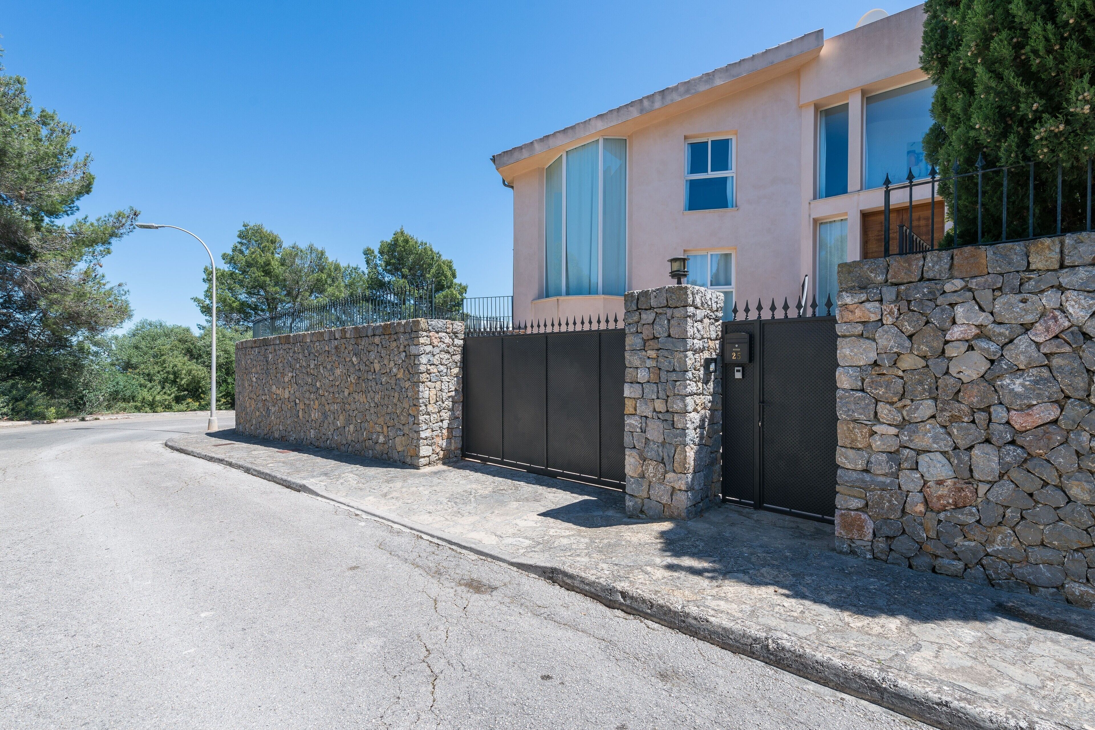 Une maison moderne avec un mur en pierre et un portail noir.